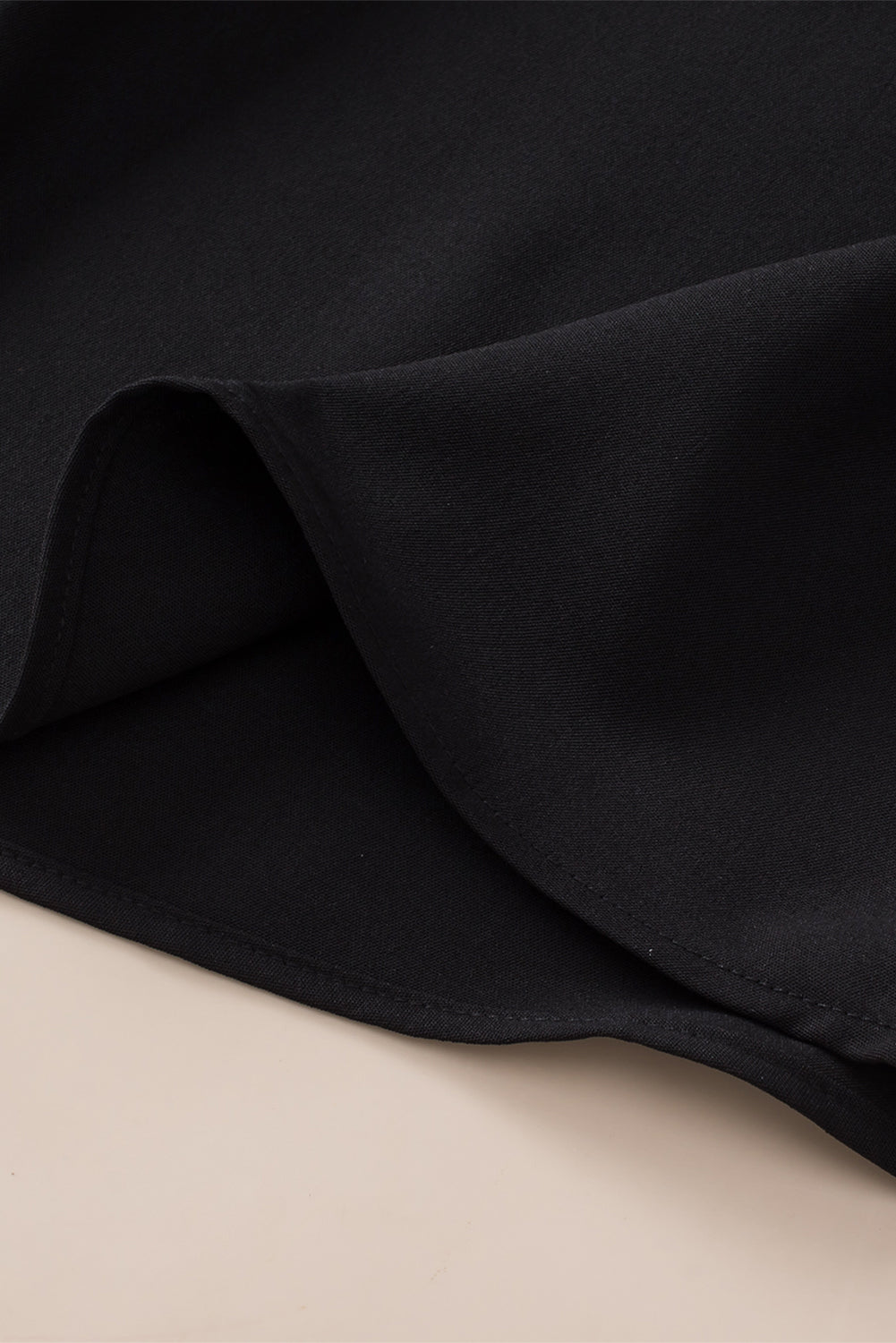 Black sleeveless tunic fabric close-up with curved hem seam