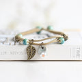 Boho ceramic bracelet with teal beads, bronze leaf pendant, and round ceramic flower charm