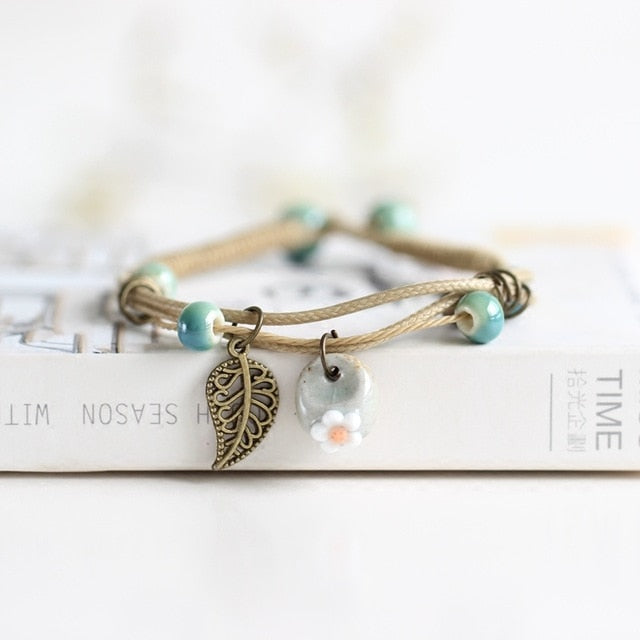 Boho ceramic bracelet with teal beads, bronze leaf pendant, and round ceramic flower charm